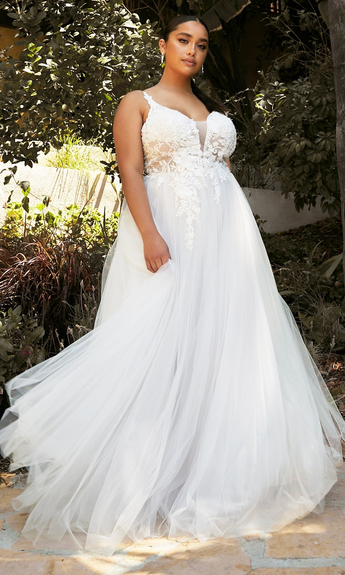 A woman stands outdoors in greenery wearing the Classic Off-White Long Prom Dress: Ladivine CB072W, which features a fitted bodice and flowing tulle skirt.